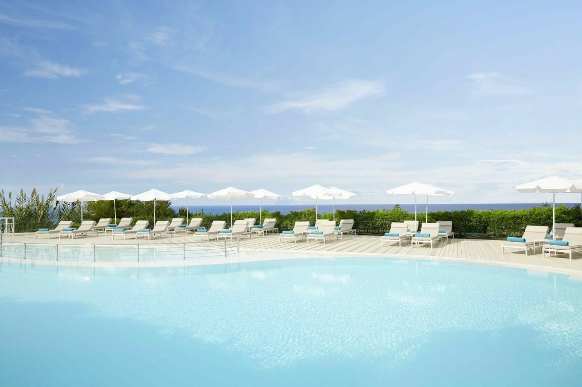 The main swimming pool set up with sunbeds and sun parasols at Pelekas Monastery, a Corfu family beach resort with a 5 star rating.